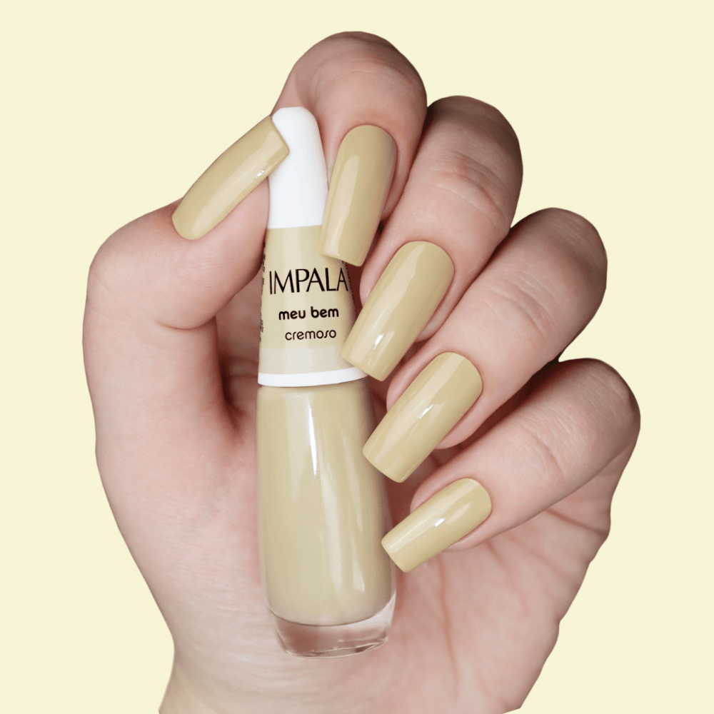 Mão segurando Esmalte Impala Meu Bem com unhas pintadas na cor nude cremoso