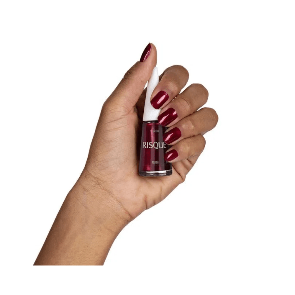 Mão segurando frasco de esmalte Risqué Rubi mostrando acabamento nas unhas