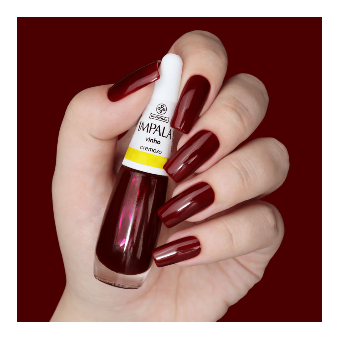 Mão com unhas pintadas de vinho segurando o frasco do esmalte Impala