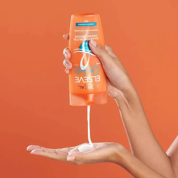 Frasco laranja do shampoo despejando produto na palma da mão mostrando textura cremosa