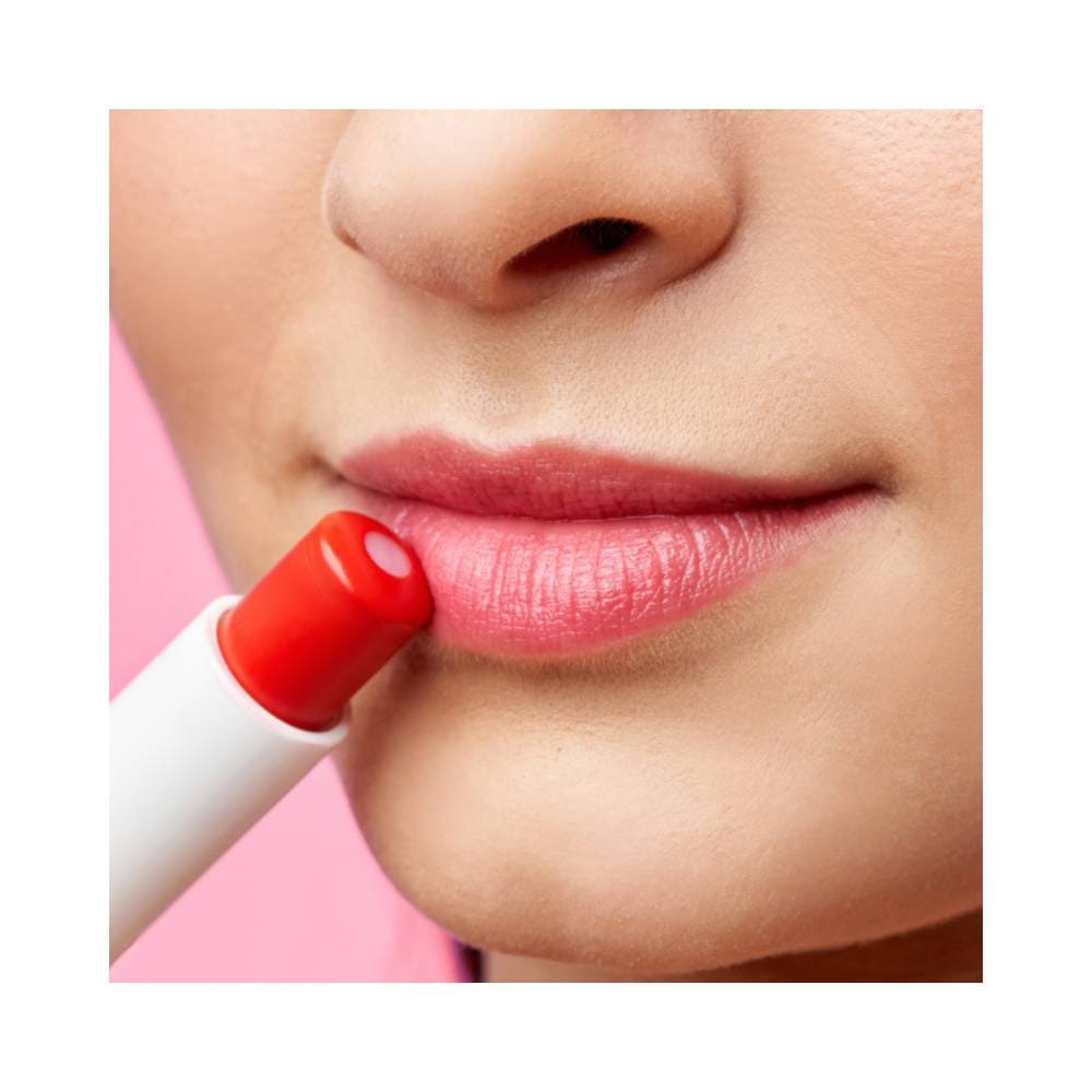 Aplicação do Balm Up Ruby Kisses próximo aos lábios em fundo rosa claro