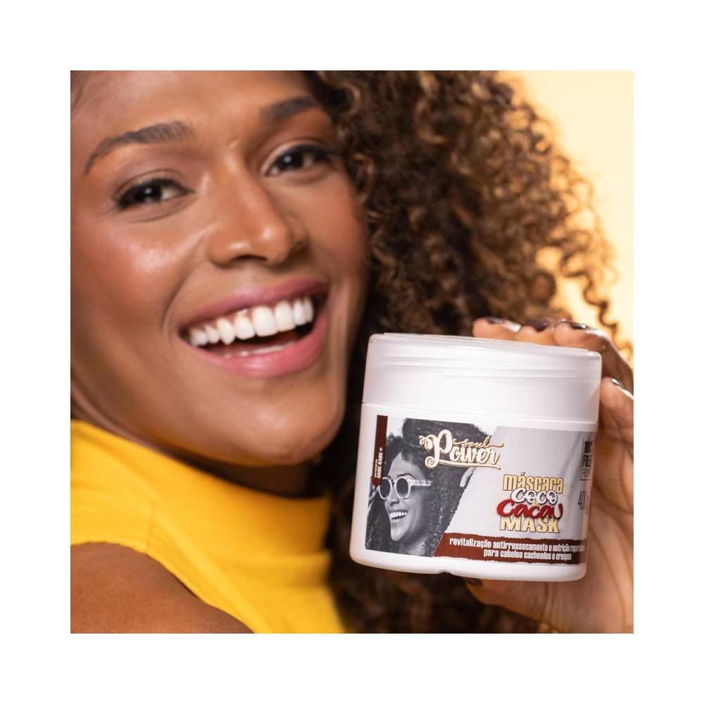 Modelo com cabelo cacheado segurando a Máscara Soul Power Coco e Cacau 400g