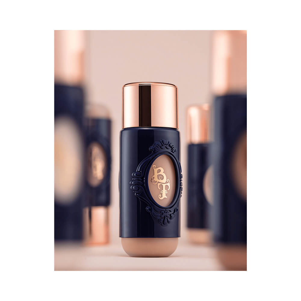 Frasco da Base Líquida Bruna Tavares Skin M20 com detalhes dourados em fundo rosa