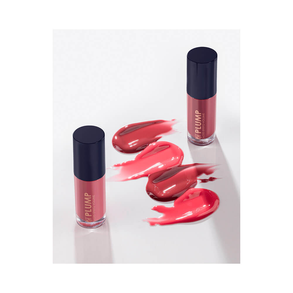 Três frascos de gloss labial em formato de lápis, cor rosa claro, sobre superfície branca.