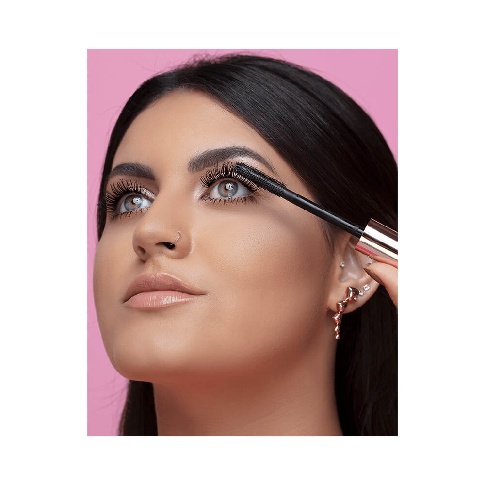 Mulher aplicando Máscara de Cílios Bruna Tavares Biglash com aplicador, destacando volume e alongamento.