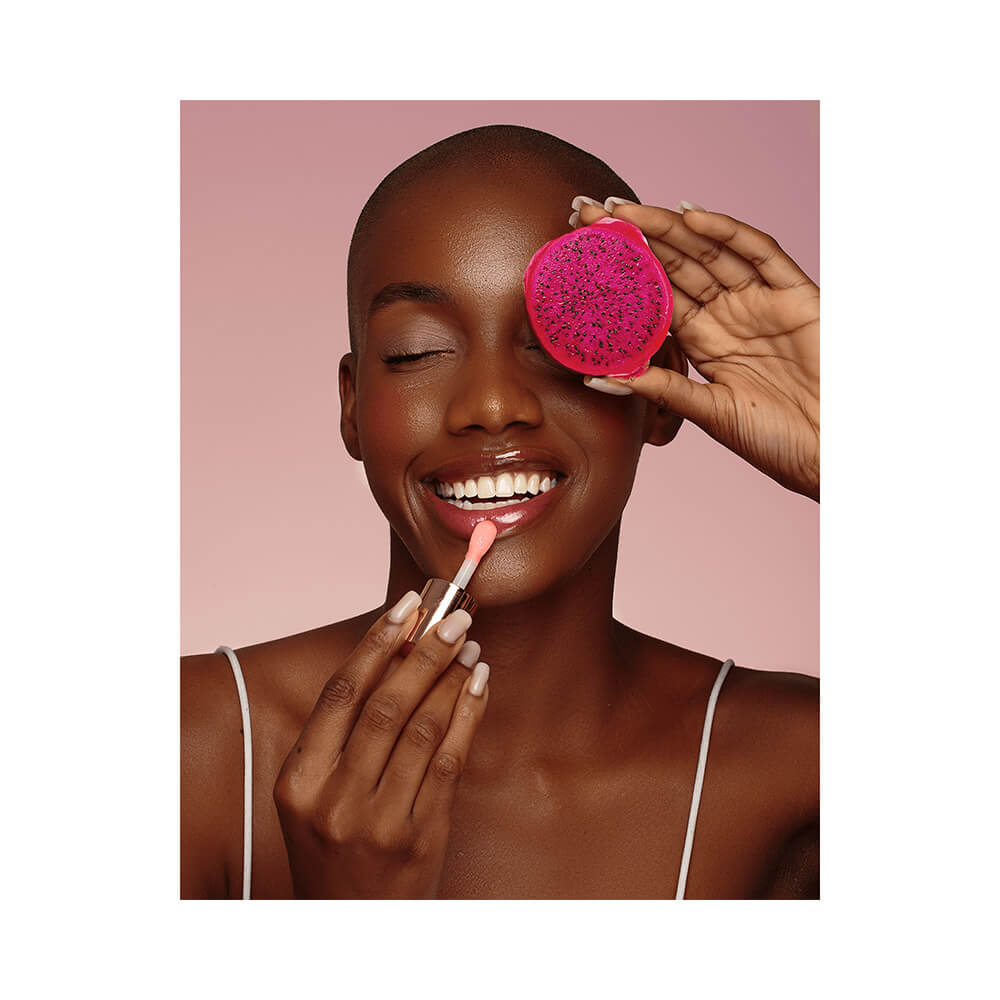 Mulher aplicando Juicy Oil Bruna Tavares Pitaya nos lábios com sorriso