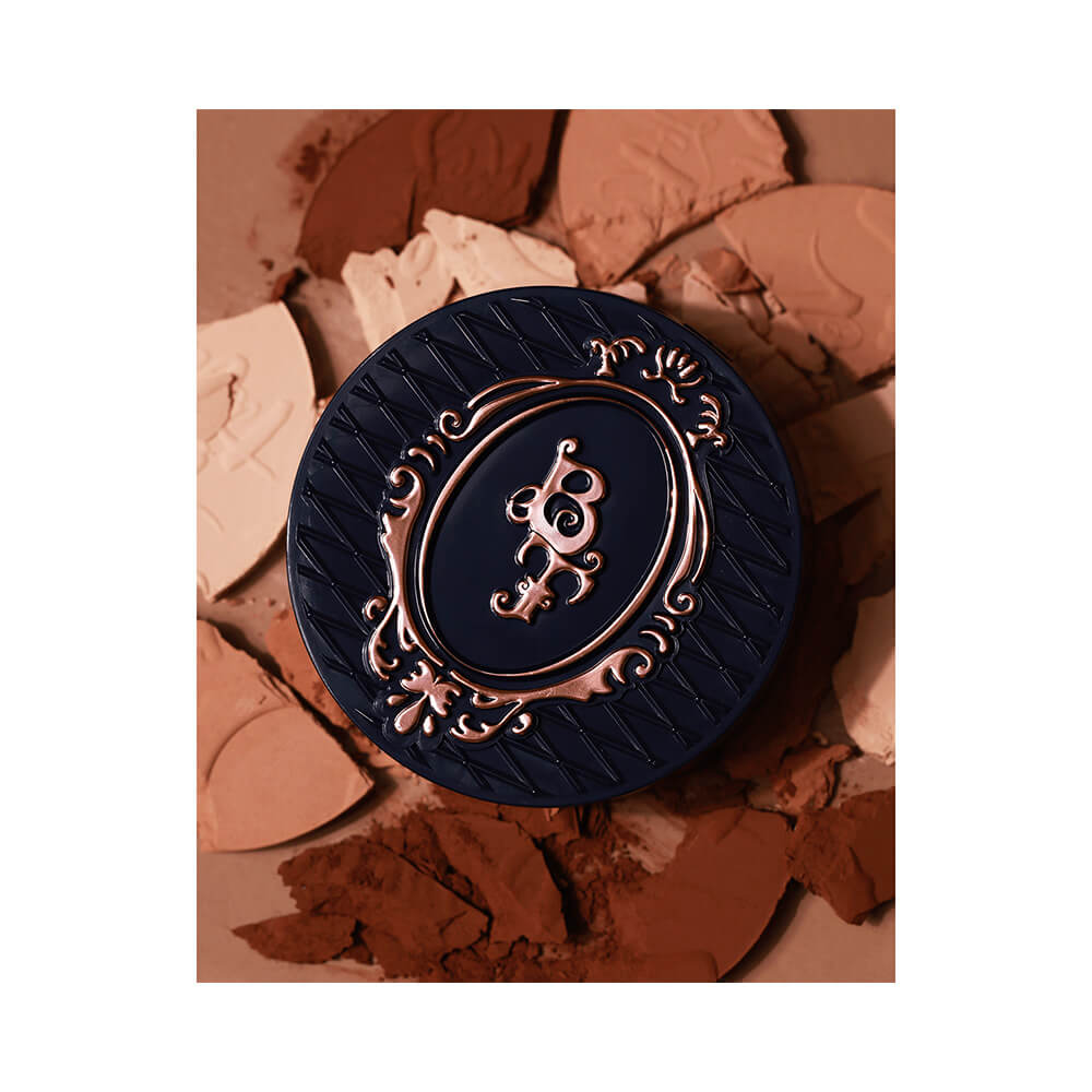 Pó Compacto Bruna Tavares Powder 20 fechado sobre fundo com pós em várias tonalidades