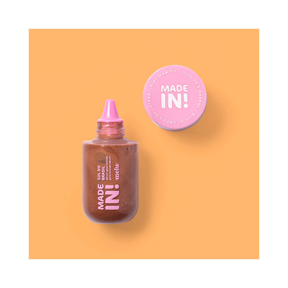 Frasco aberto do corretivo líquido Melu Made In! tom marrom bronze com aplicador de ponta fina rosa e ingredientes destacados ao redor.