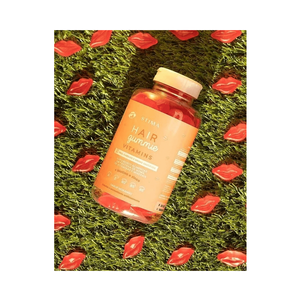 Frasco Stima Hair Gummie Vitamins sobre grama artificial exibindo gomas em formato de lábios