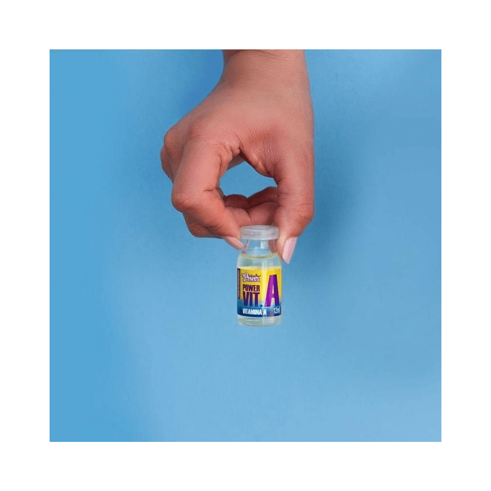 Mão segurando ampola Soul Power Vitamina A 12ml com líquido amarelo, fundo azul claro