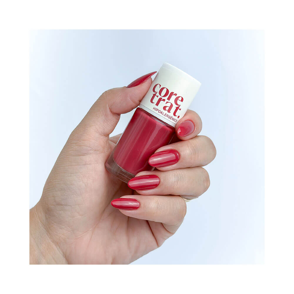 Mão feminina com unhas pintadas de vermelho canela segurando o esmalte Blant Coretrat