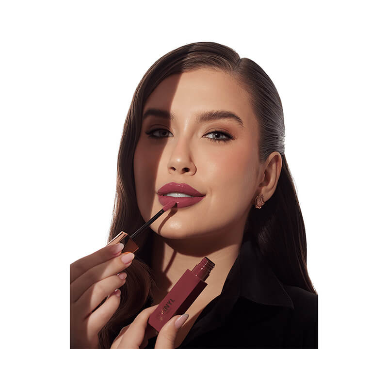 Mulher usando Batom Líquido Bruna Tavares Vinyl Livia, destacando a cor vinho profundo nos lábios.