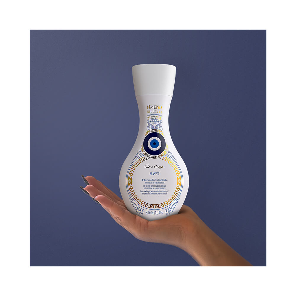 Mão segurando o frasco do Shampoo Amend Millenar Óleos Gregos 300ml com fundo azul escuro