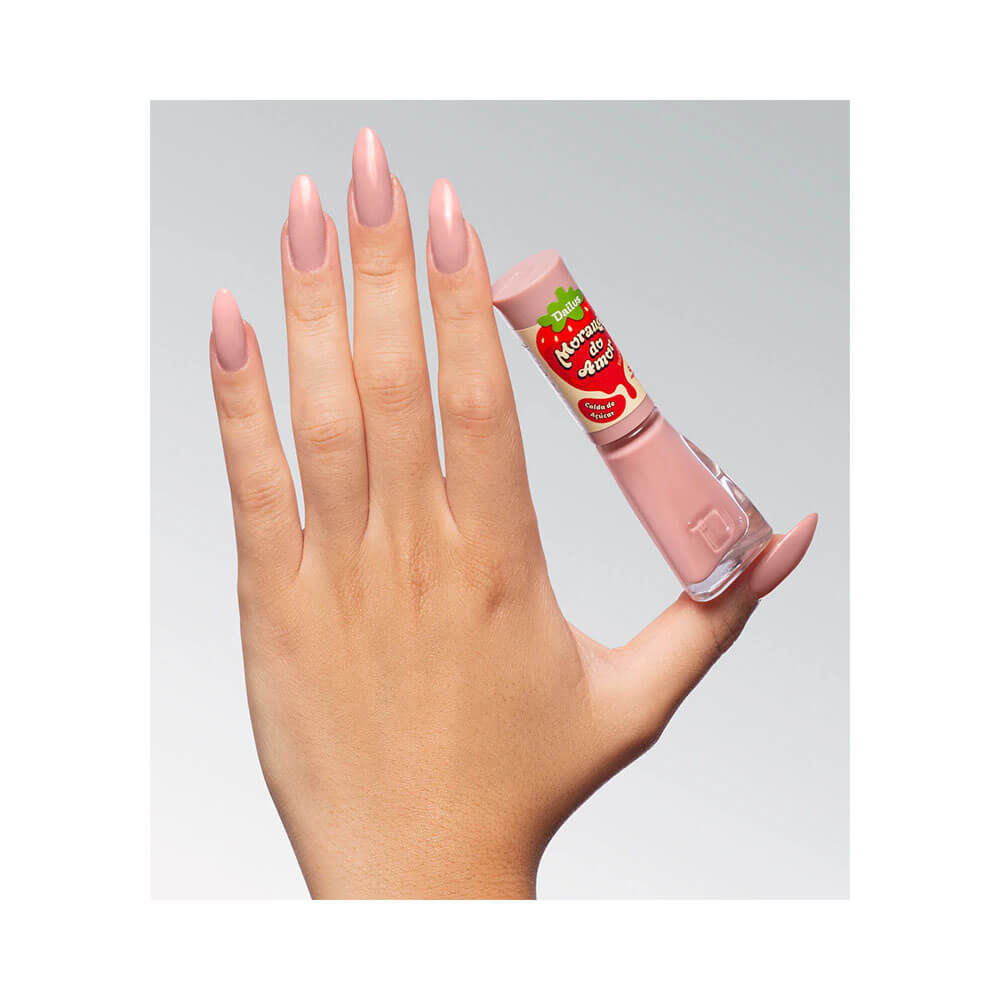 Mão segurando esmalte Dailus Morango do Amor Calda de Açúcar com unhas pintadas de rosa claro