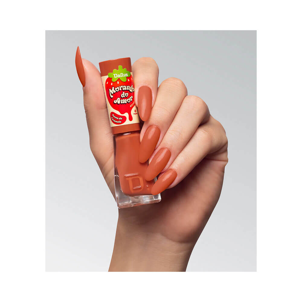 Mão com unhas pintadas na cor Ponto de Caramelo segurando o esmalte Dailus.