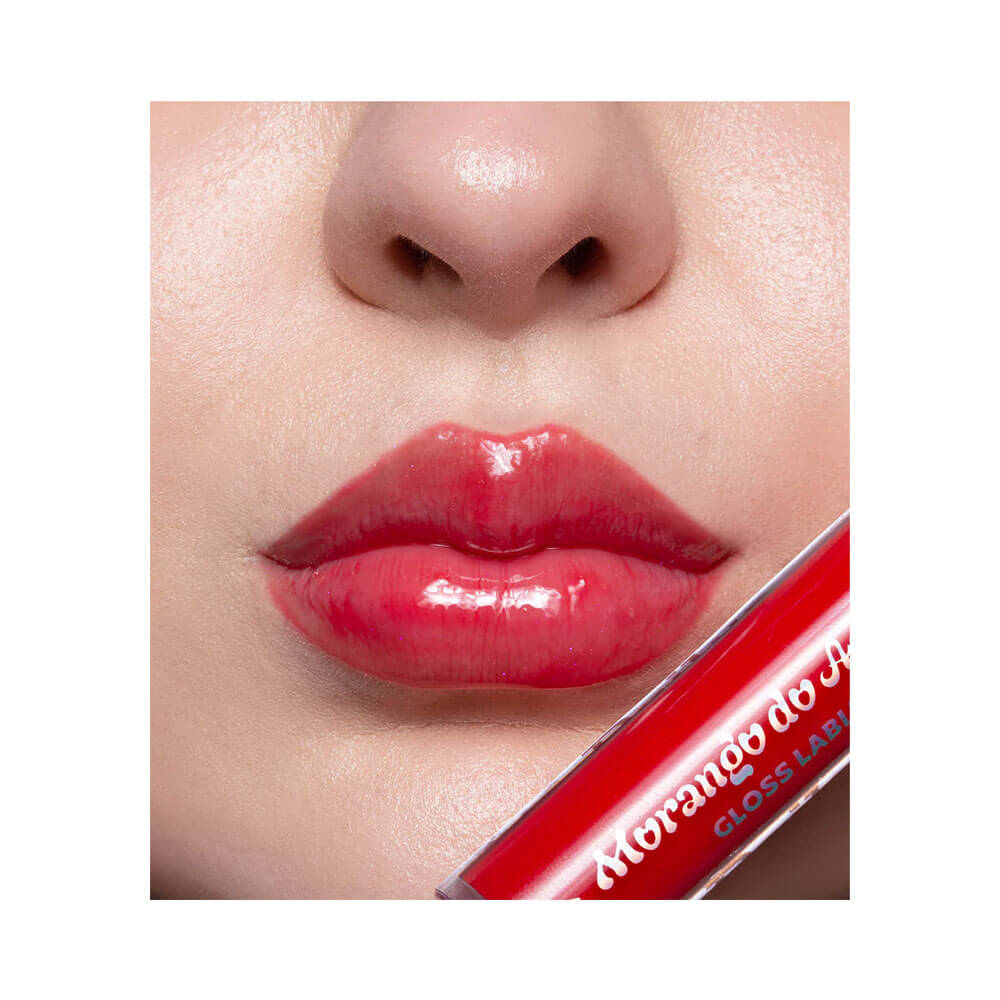 Close nos lábios com aplicação uniforme do Lip Gloss Dailus Morango do Amor Morangão, brilho intenso e translúcido.