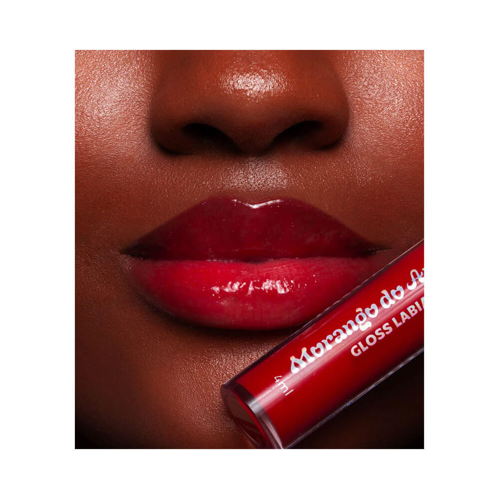 Close nos lábios com gloss vermelho intenso e brilhante aplicado, mostrando textura e cor.