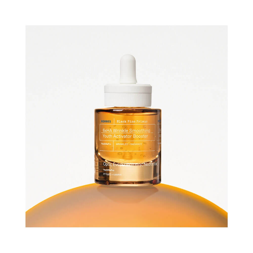 Frasco âmbar translúcido do Sérum Facial Korres Black Pine Primus Booster Antirrugas sobre superfície laranja