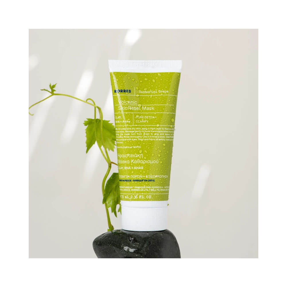 Máscara Korres Santorini Grape sobre pedra preta com planta verde ao fundo