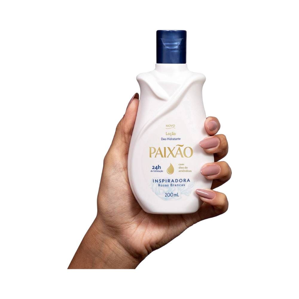 Mão segurando o hidratante Paixão Inspiradora com Óleo de Amêndoas, embalagem branca com tampa azul escura.