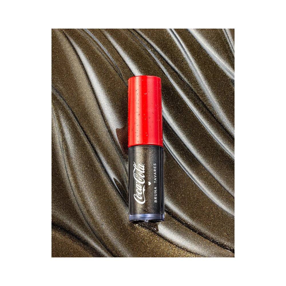 Detalhe da embalagem do Lip Gloss Sérum Bruna Tavares Coca-Cola Black Bubbles com fundo dourado