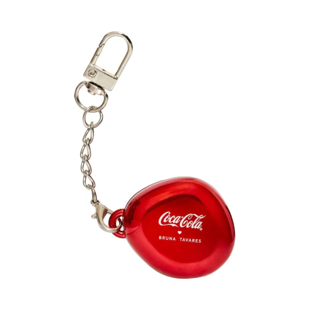 Balm labial Bruna Tavares Coca-Cola Pop Charm em forma de coração com cadeado prateado e corrente, aberto mostrando o produto vermelho sobre fundo vermelho com linhas brancas