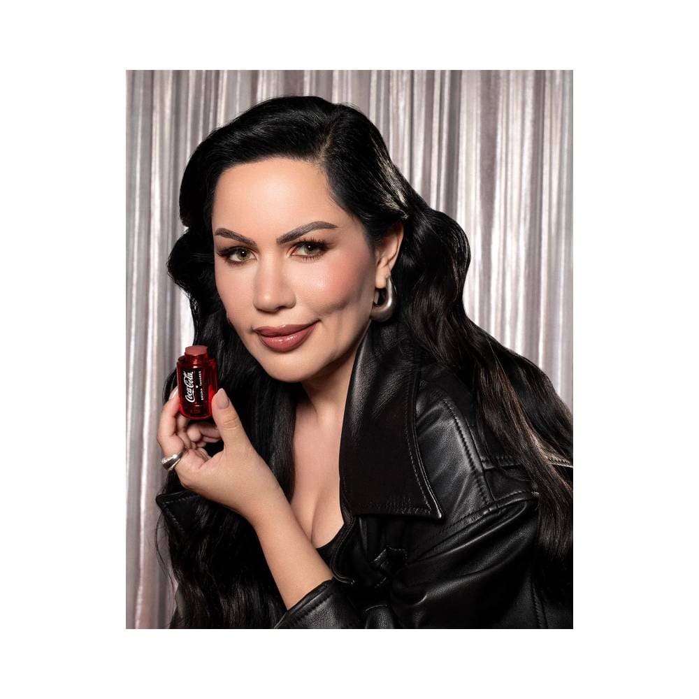 Mulher segurando Blush Stick Bruna Tavares Coca-Cola Classic Brown com fundo prateado