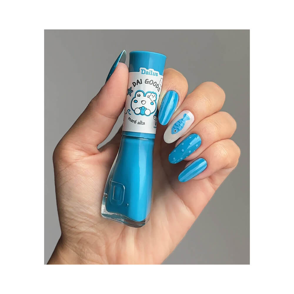 Mão segurando esmalte Dailus Dai Goods Maré Alta com unhas decoradas em azul vibrante e detalhes brancos.