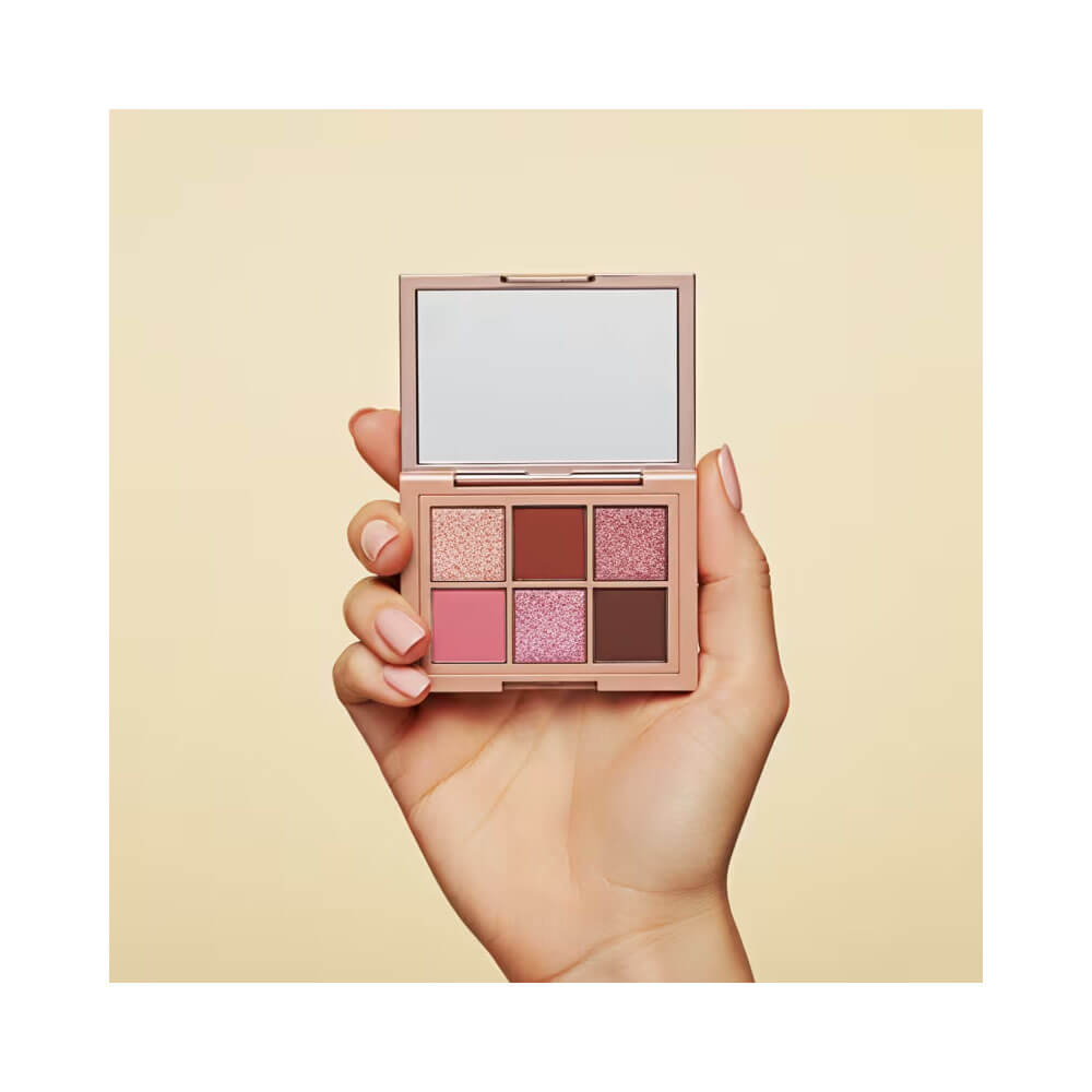 Mão segurando paleta de sombras Niina Secrets Rosé Shine aberta com espelho refletindo