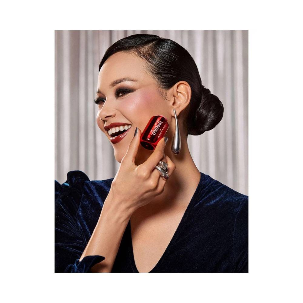 Mulher sorrindo aplicando Blush Stick Bruna Tavares Coca-Cola Flush Vibes nos lábios