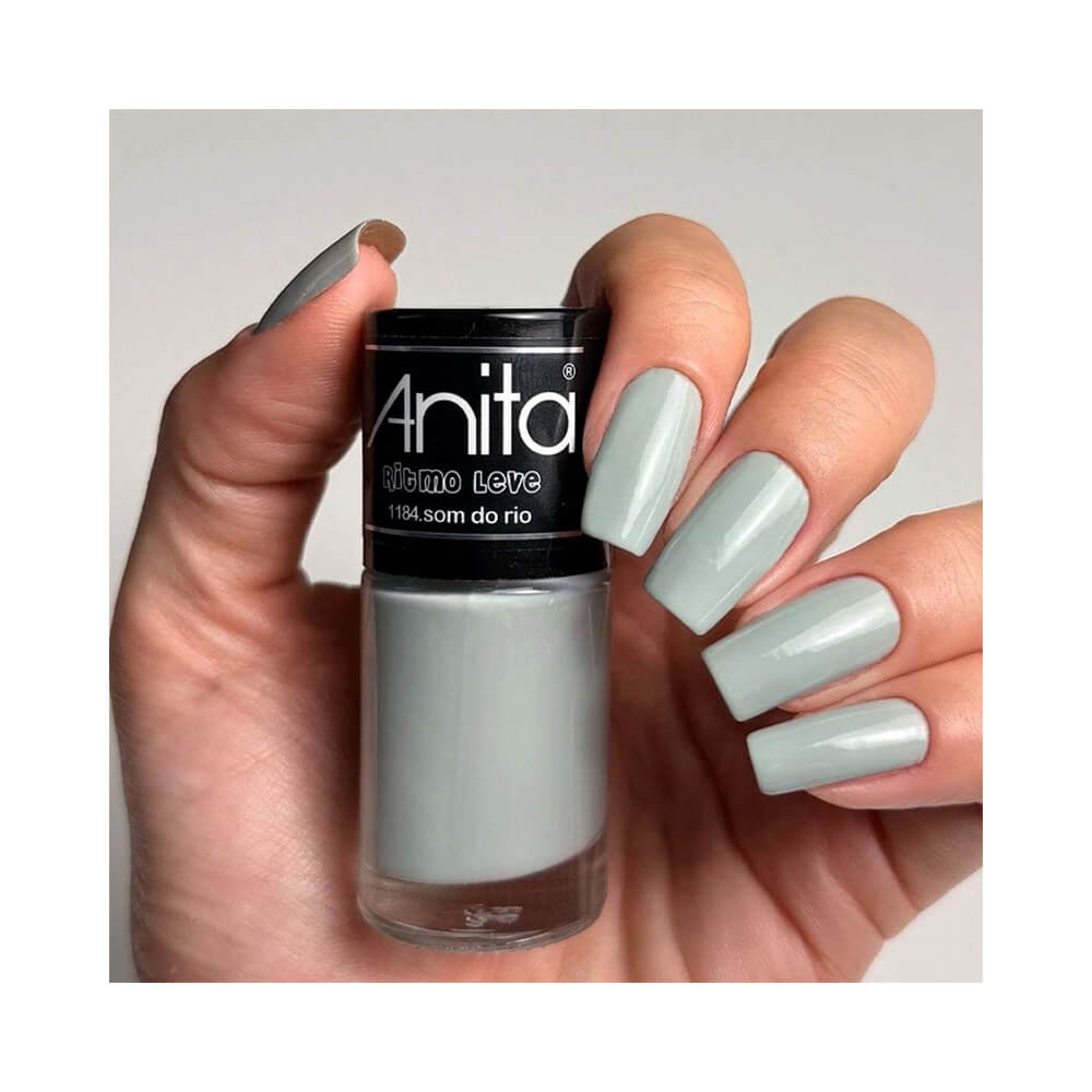 Mão feminina segurando o esmalte Anita Ritmo Leve Som do Rio, mostrando unhas pintadas com cor verde suave e brilho