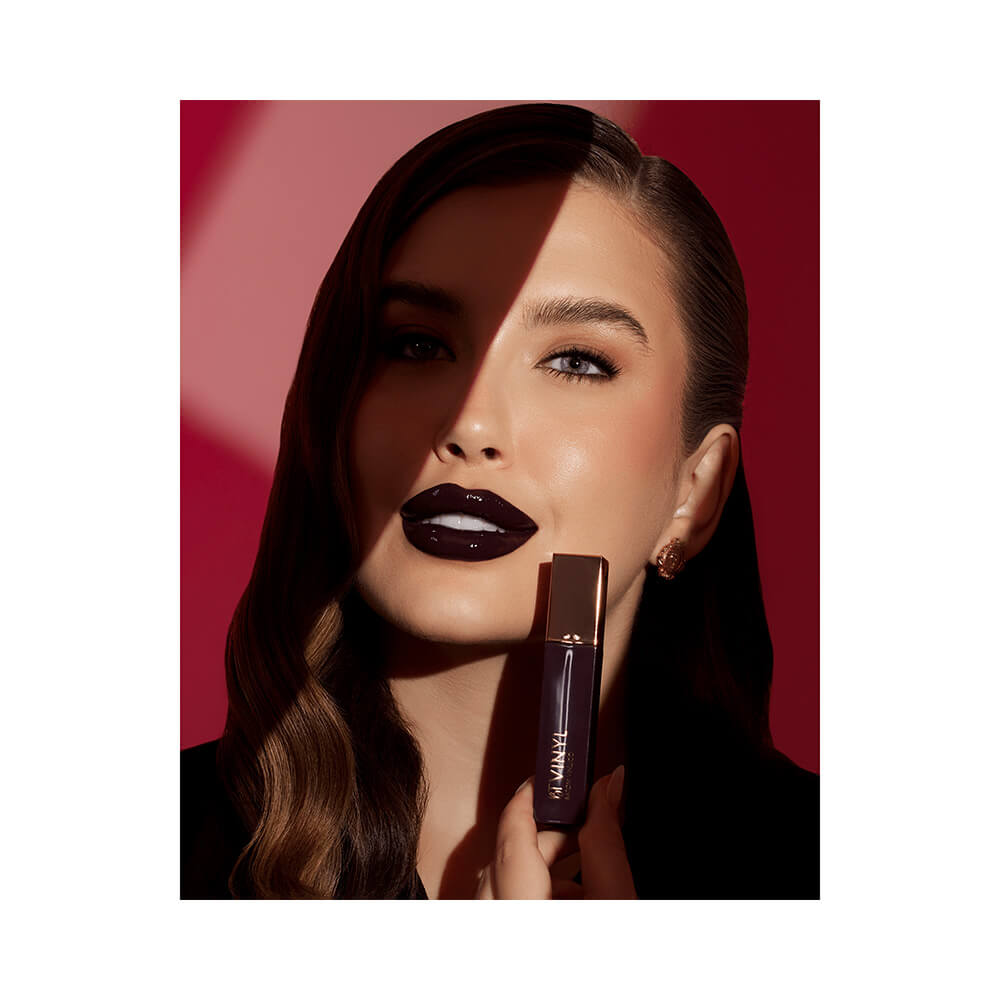 Mulher com batom líquido Bruna Tavares Vinyl Morgana cor roxa profunda aplicado nos lábios.