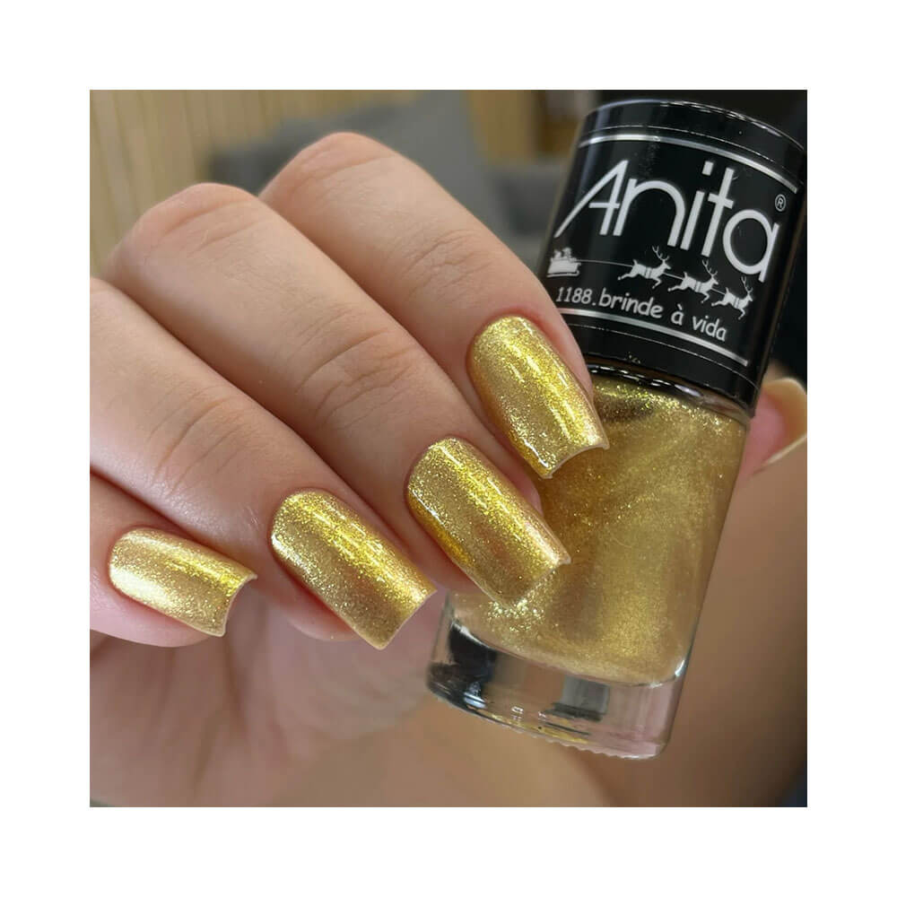 Mão feminina segurando o esmalte Anita Tempo de Celebrar Brinde à Vida com unhas pintadas na mesma cor dourada