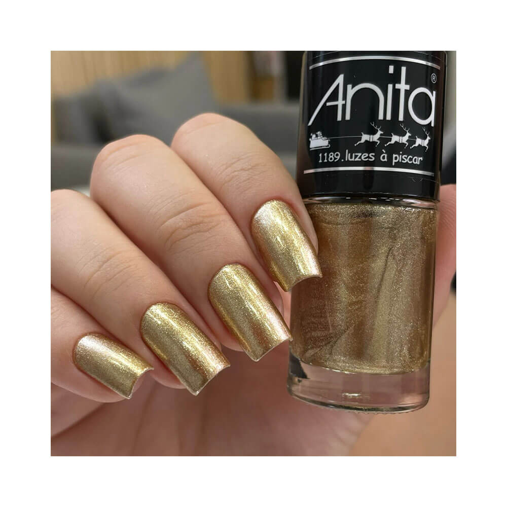 Aplicação do esmalte Anita Luzes à Piscar nas unhas, mostrando brilho dourado metálico