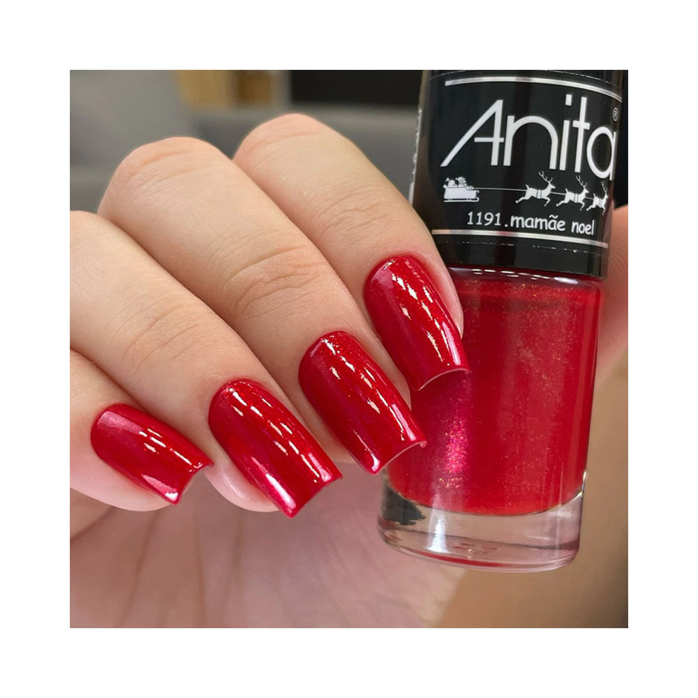 Mão feminina segurando esmalte Anita Tempo de Celebrar Mamãe Noel com unhas pintadas de vermelho brilhante