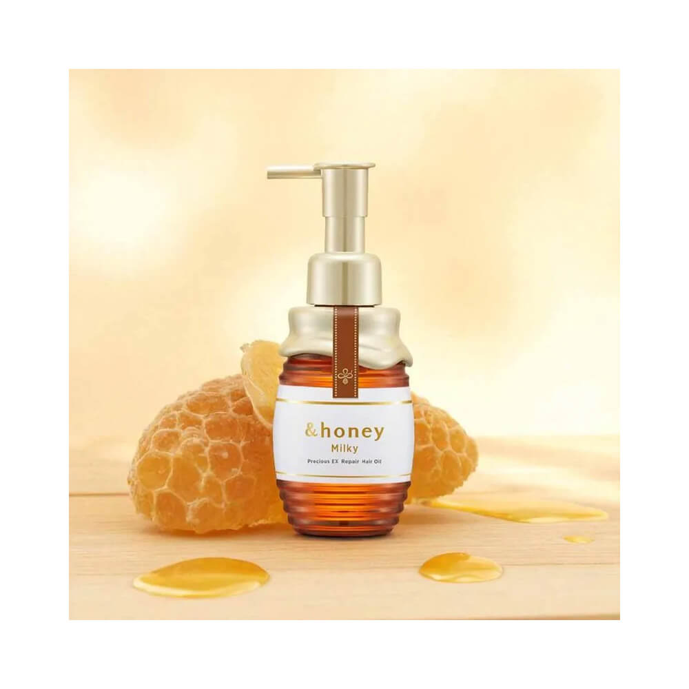 Frasco do óleo capilar &Honey Milky Precious Ex Repair 105ml posicionado sobre superfície de madeira clara com favo de mel ao fundo