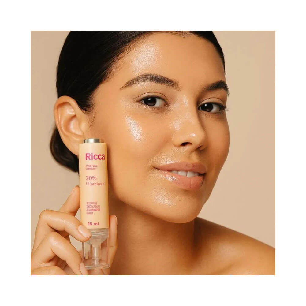 Mulher com pele iluminada segurando o Sérum Facial Ricca Vitamina C Iluminador 15ml próximo ao rosto