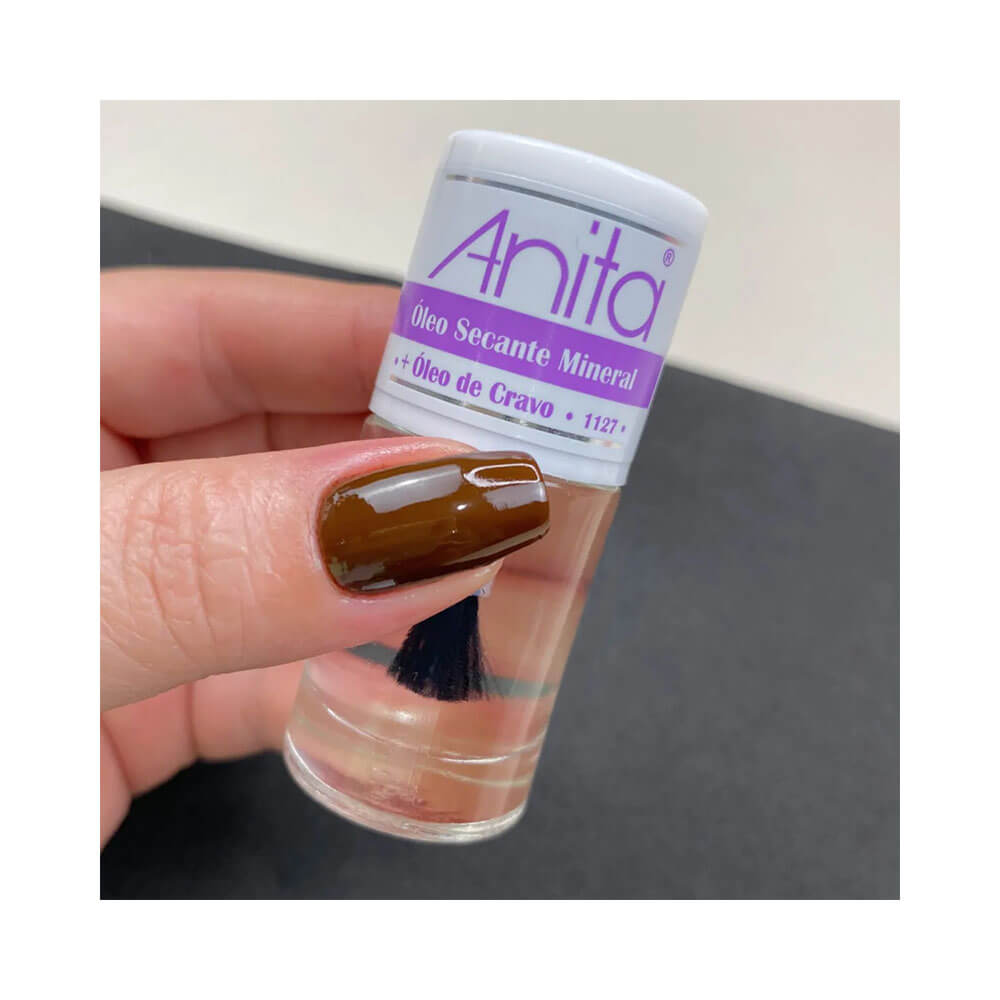 Mão segurando frasco transparente de Óleo Secante Mineral Anita com Óleo de Cravo, unha pintada em marrom brilhante