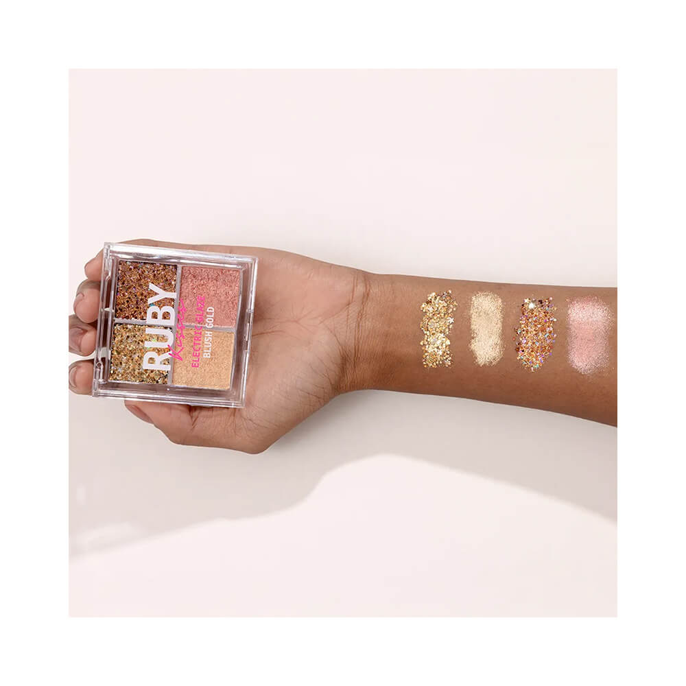 Mão segurando a paleta Ruby Kisses Electric Glaze Blush Gold com amostras das quatro cores aplicadas no braço.