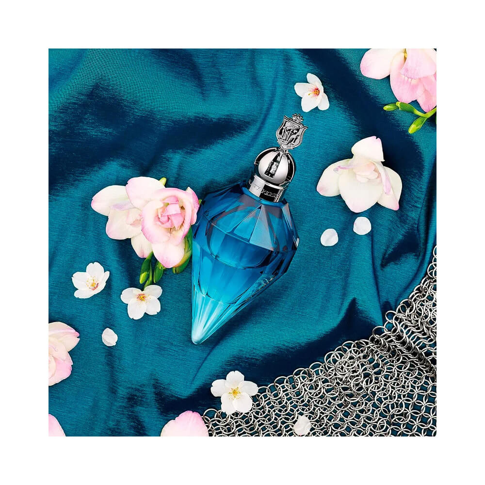 Frasco de perfume azul transparente sobre tecido azul com flores brancas e rosa